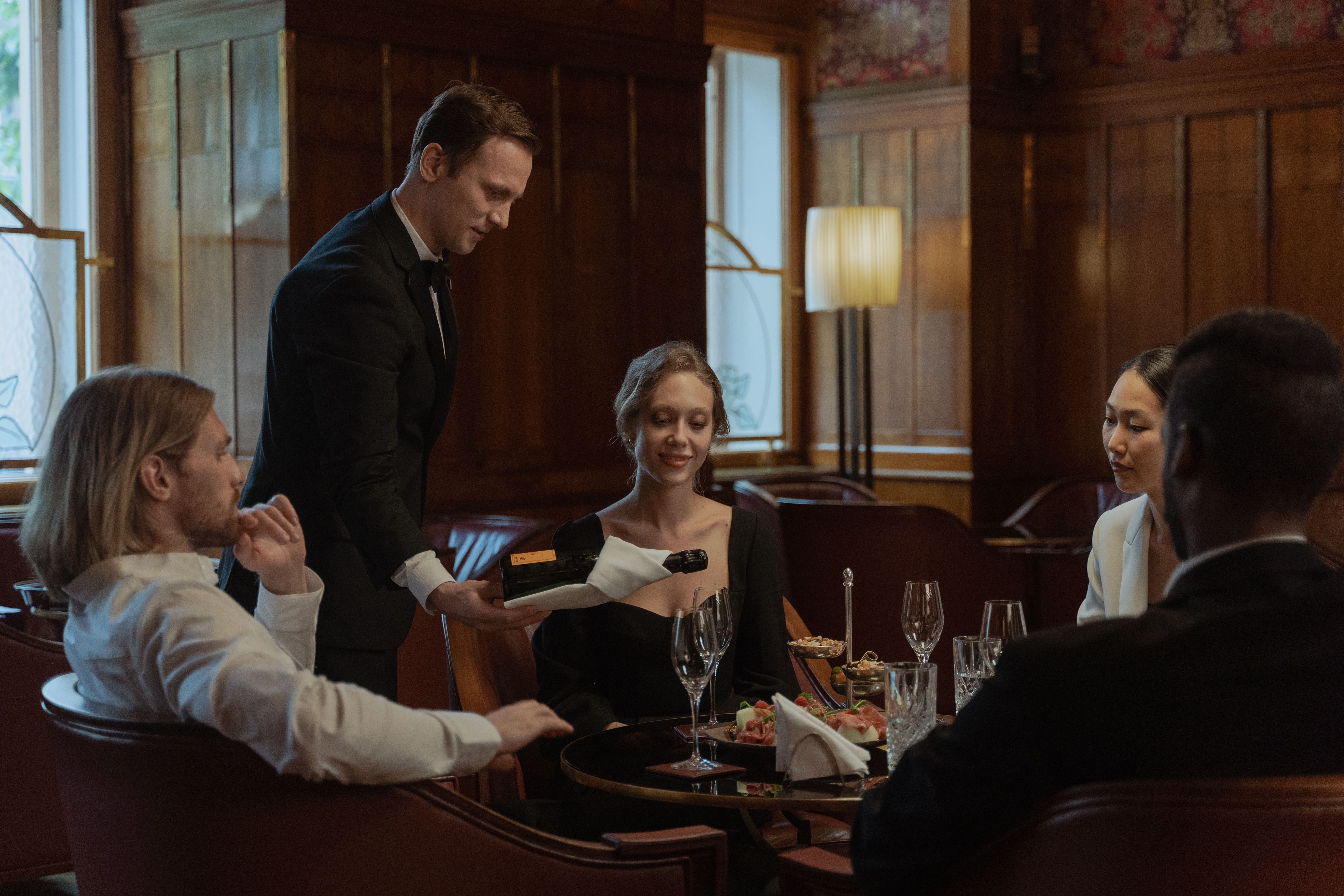Waiter serves wine to a group enjoying an elegant meal at an upscale restaurant