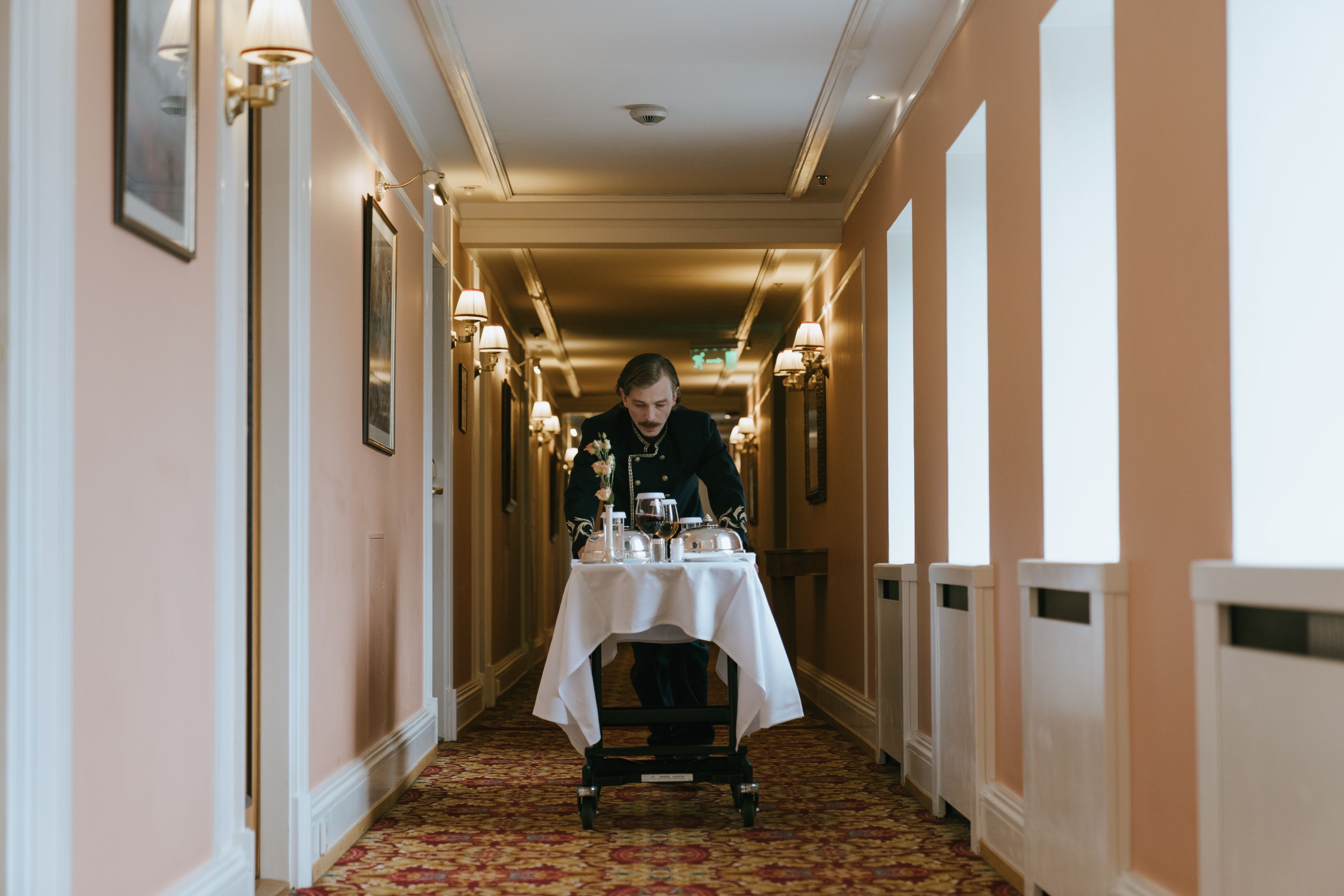 Hotel staff member pushes a room service trolley through a luxurious corridor