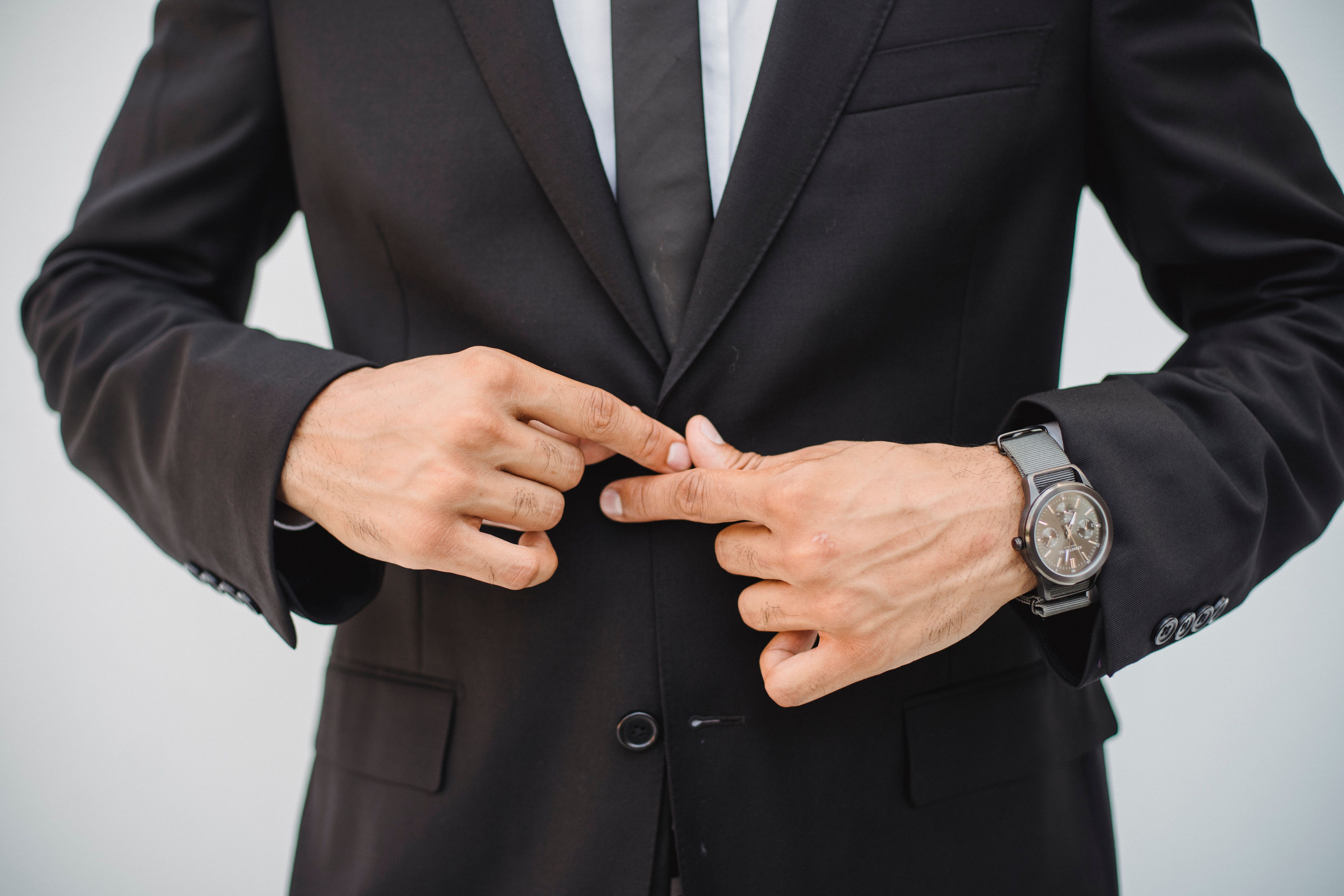 Close-up of a man's hands adjusting a tailored black suit jacket, reflecting care and self-worth