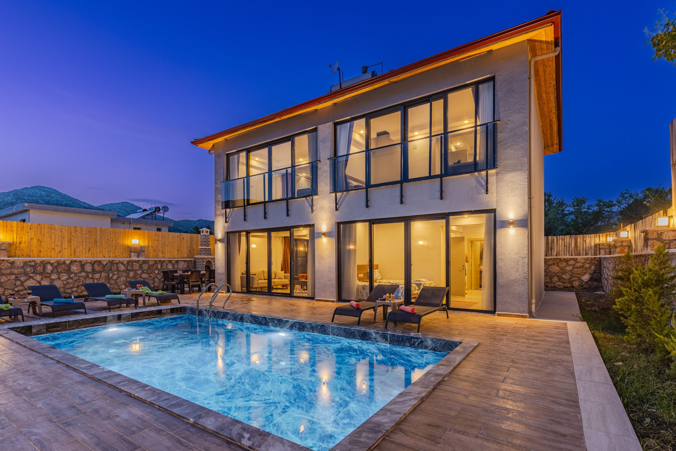 Modern luxury celebrity-style home with illuminated infinity pool and patio at dusk