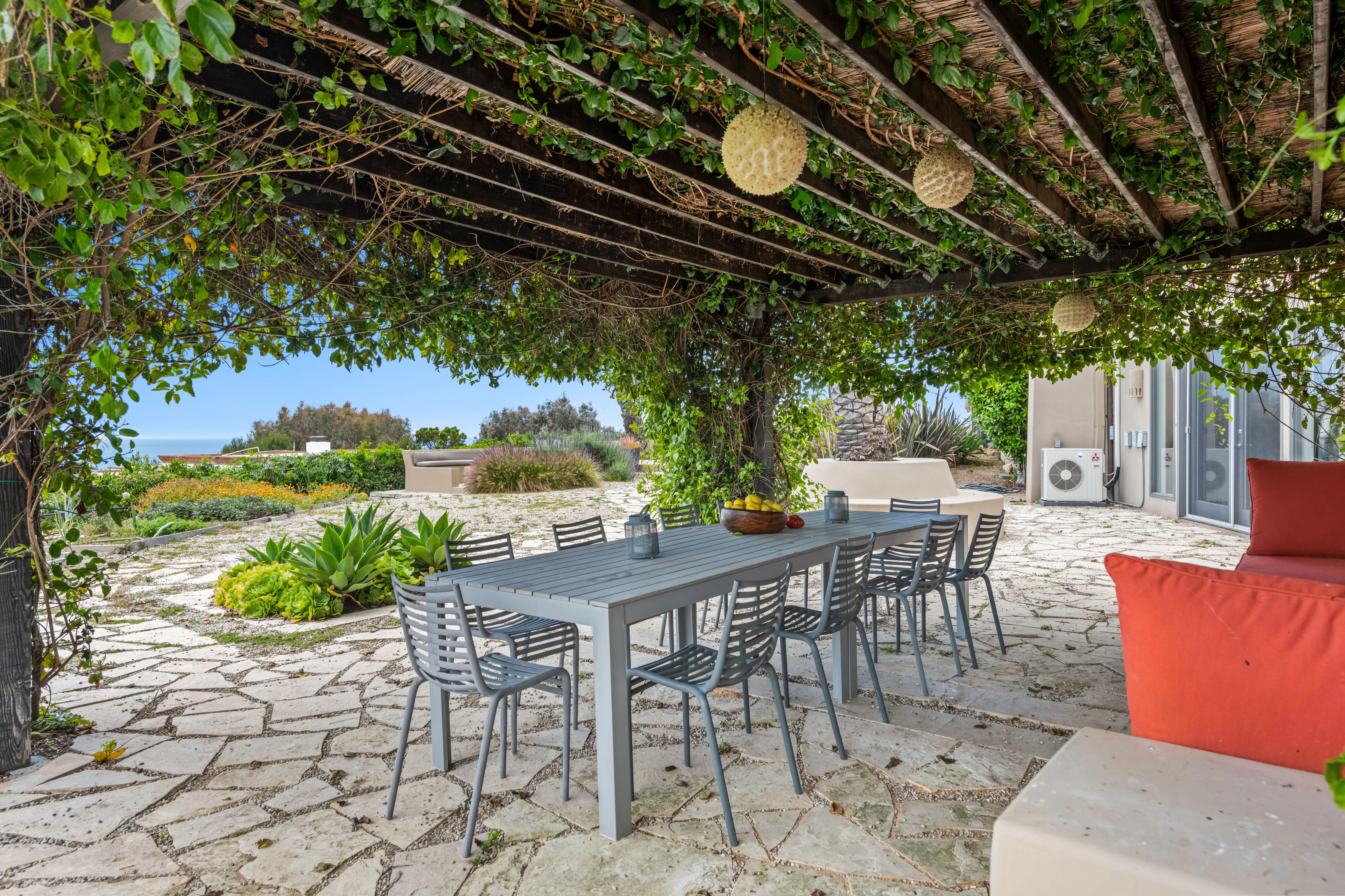 Elegant garden dining patio under a vine-covered pergola with an ocean view